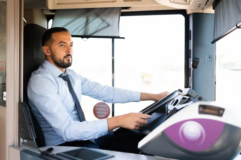 Conducteur de bus à son poste de conduite, tenant le volant et regardant tout droit.